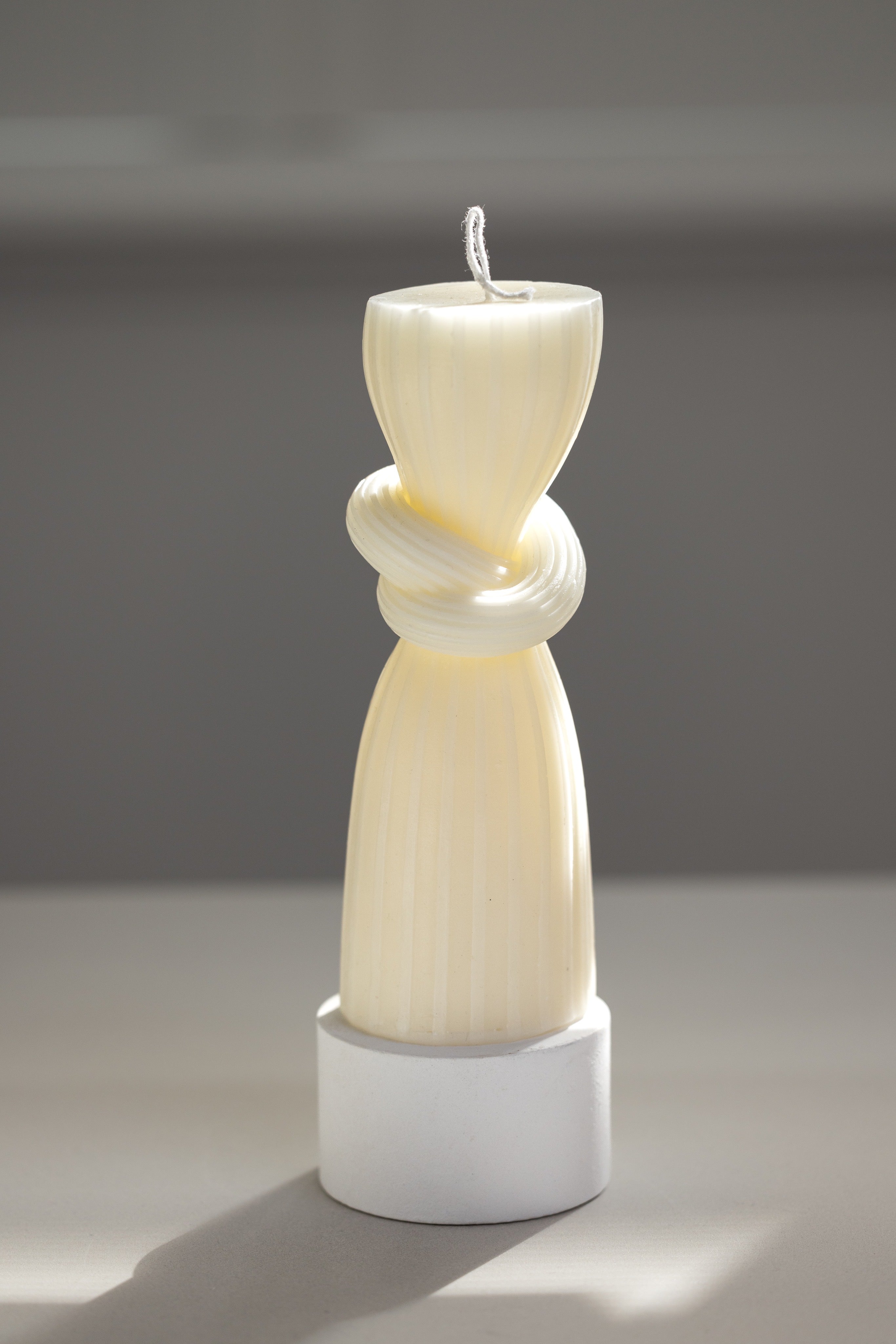 Cream sculptural soy candle with a tiered abstract silhouette, displayed on a white ceramic tray.