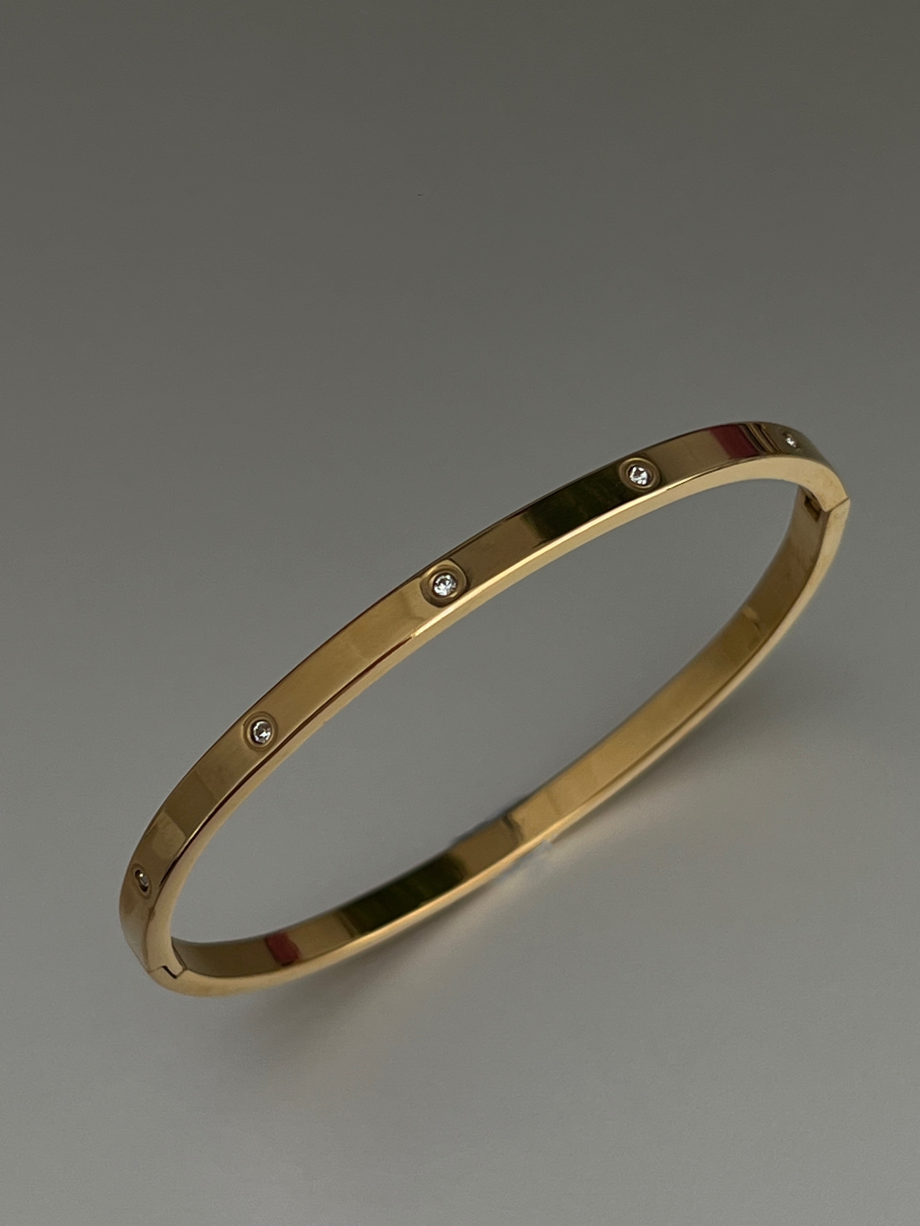 Minimal gold cuff bracelet with subtle detailing, displayed upright on a neutral surface.