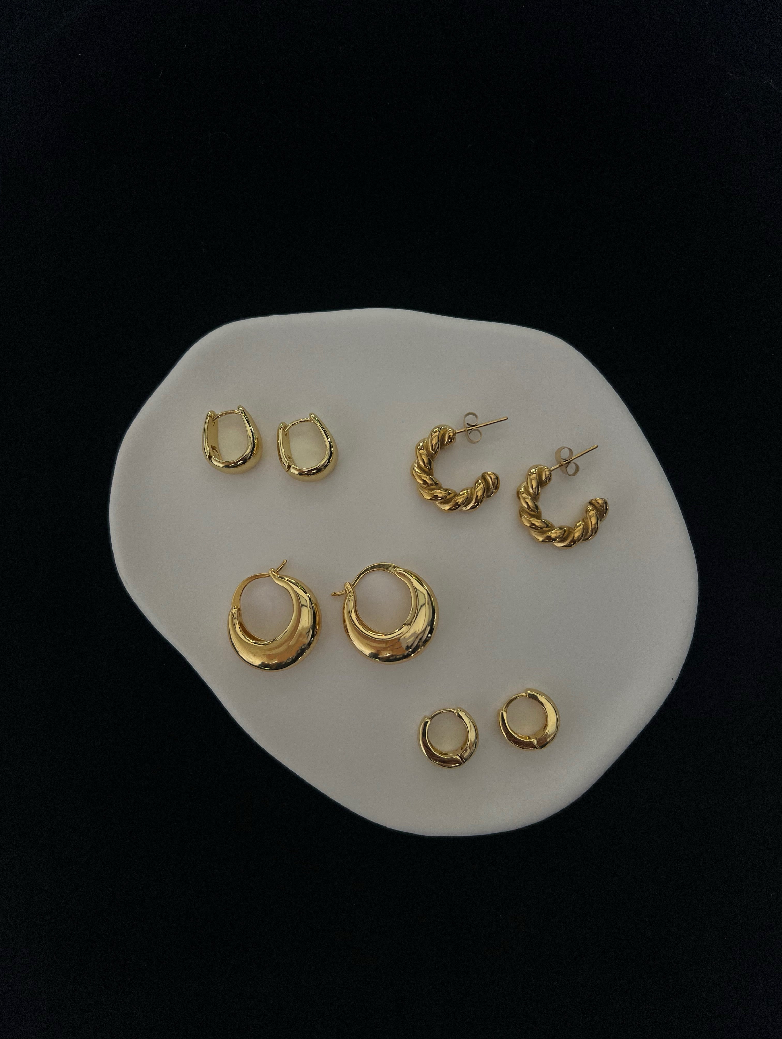 Minimal gold EverLuxe earrings arranged on a ceramic plate, photographed with a clean, black background.