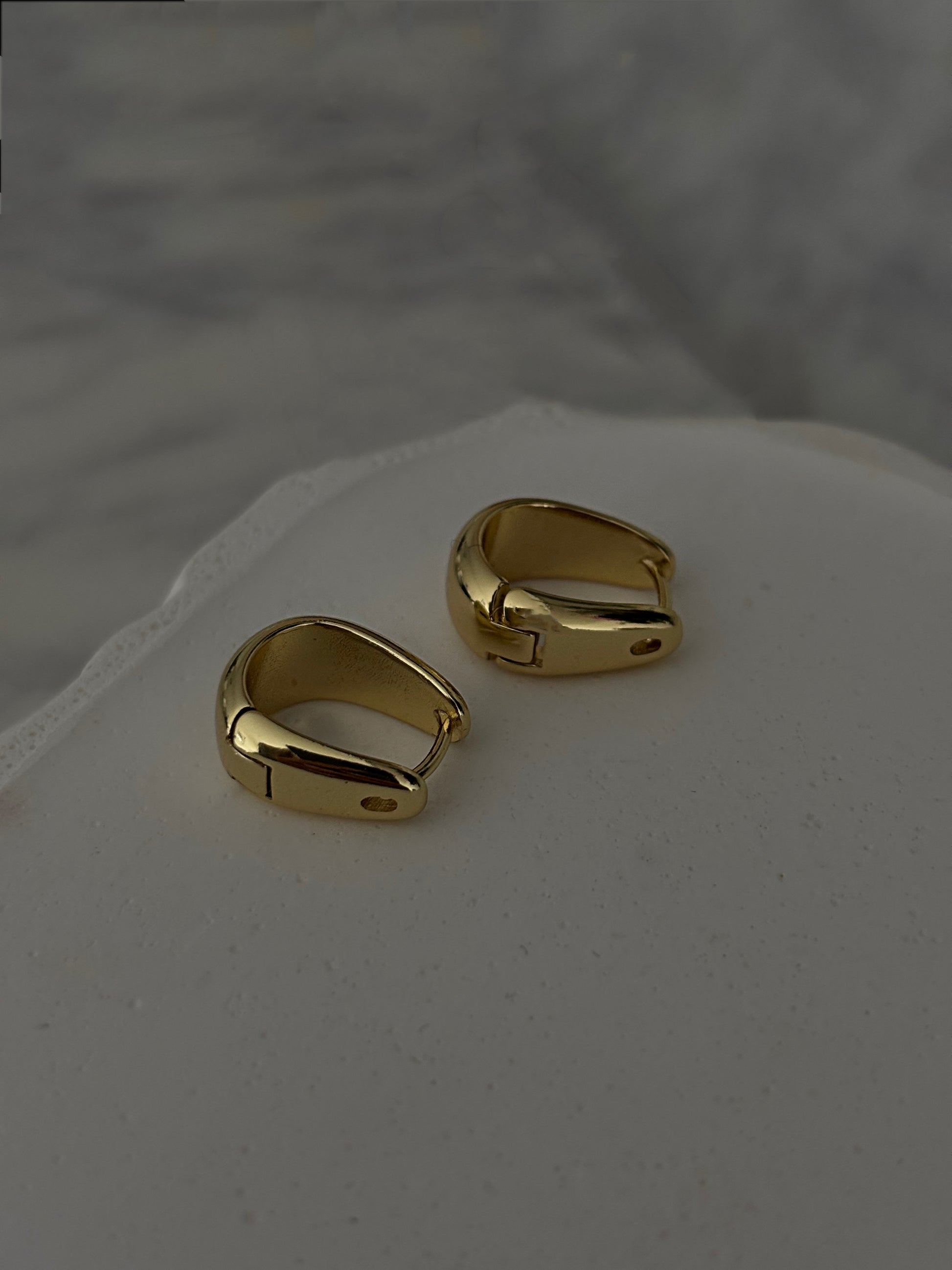 Pair of gold hoop earrings on a light gray surface with a blurred background
