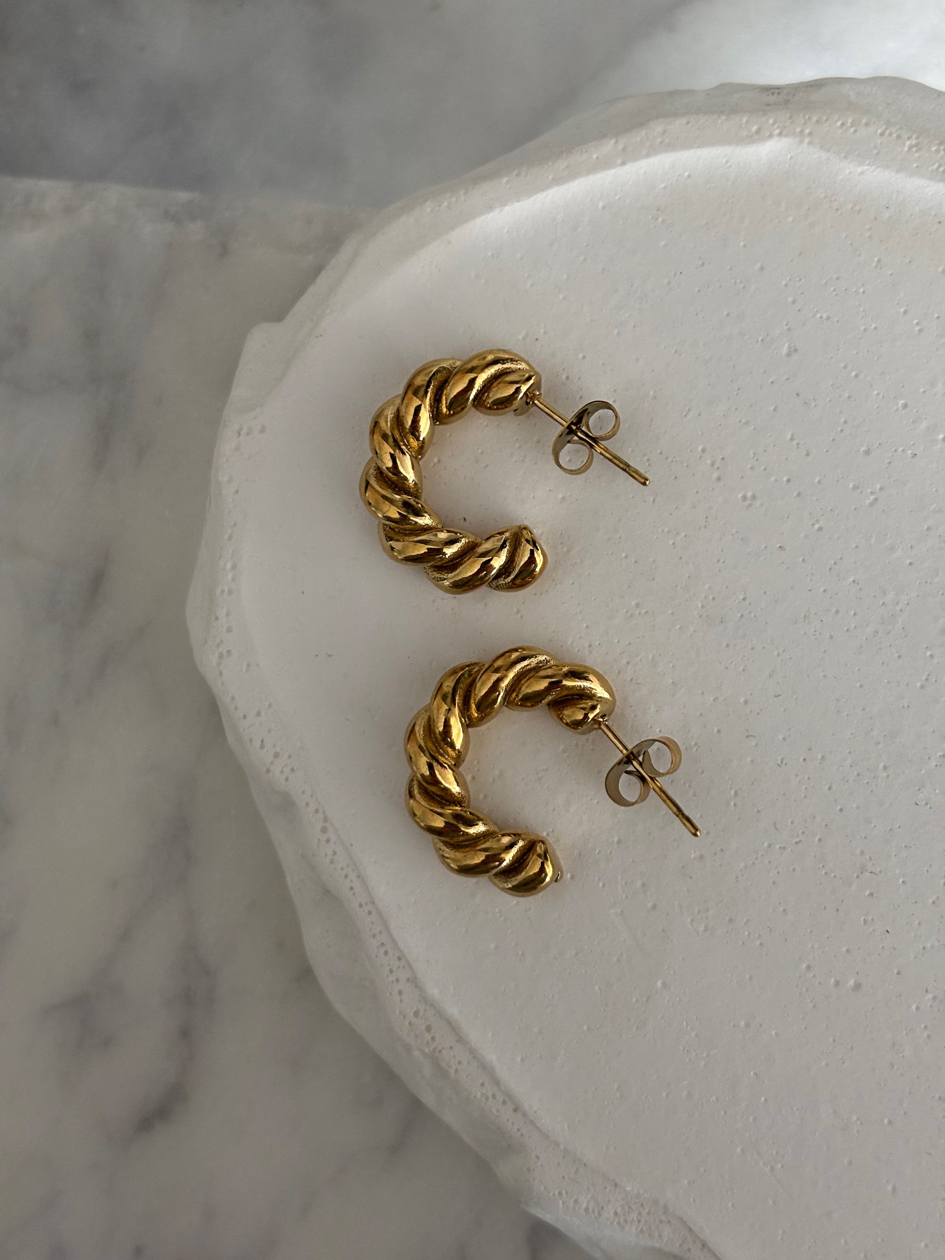 Gold hoop earrings on a white stone surface