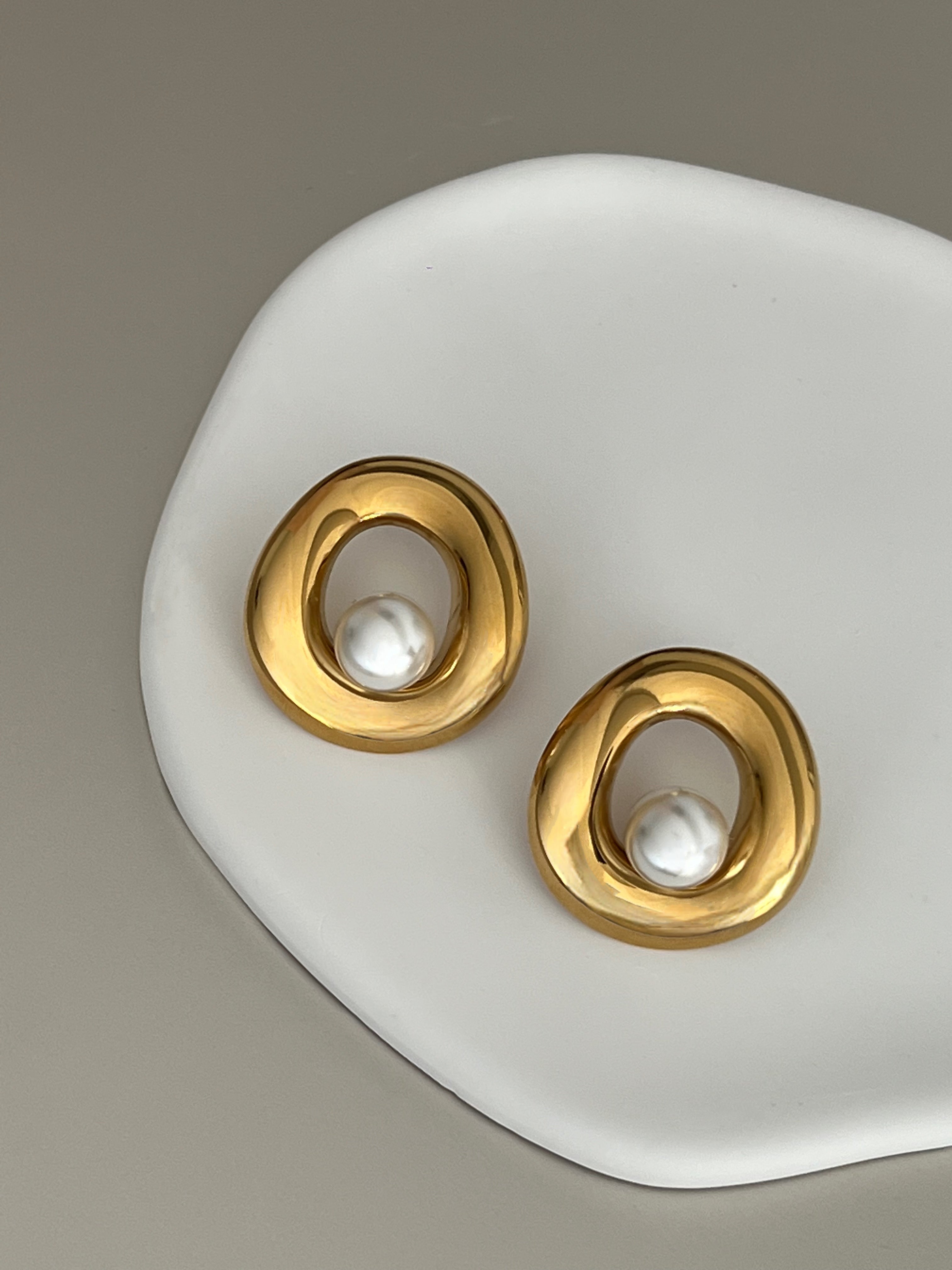 Gold earrings with pearl centers on a white stand against a gray background.