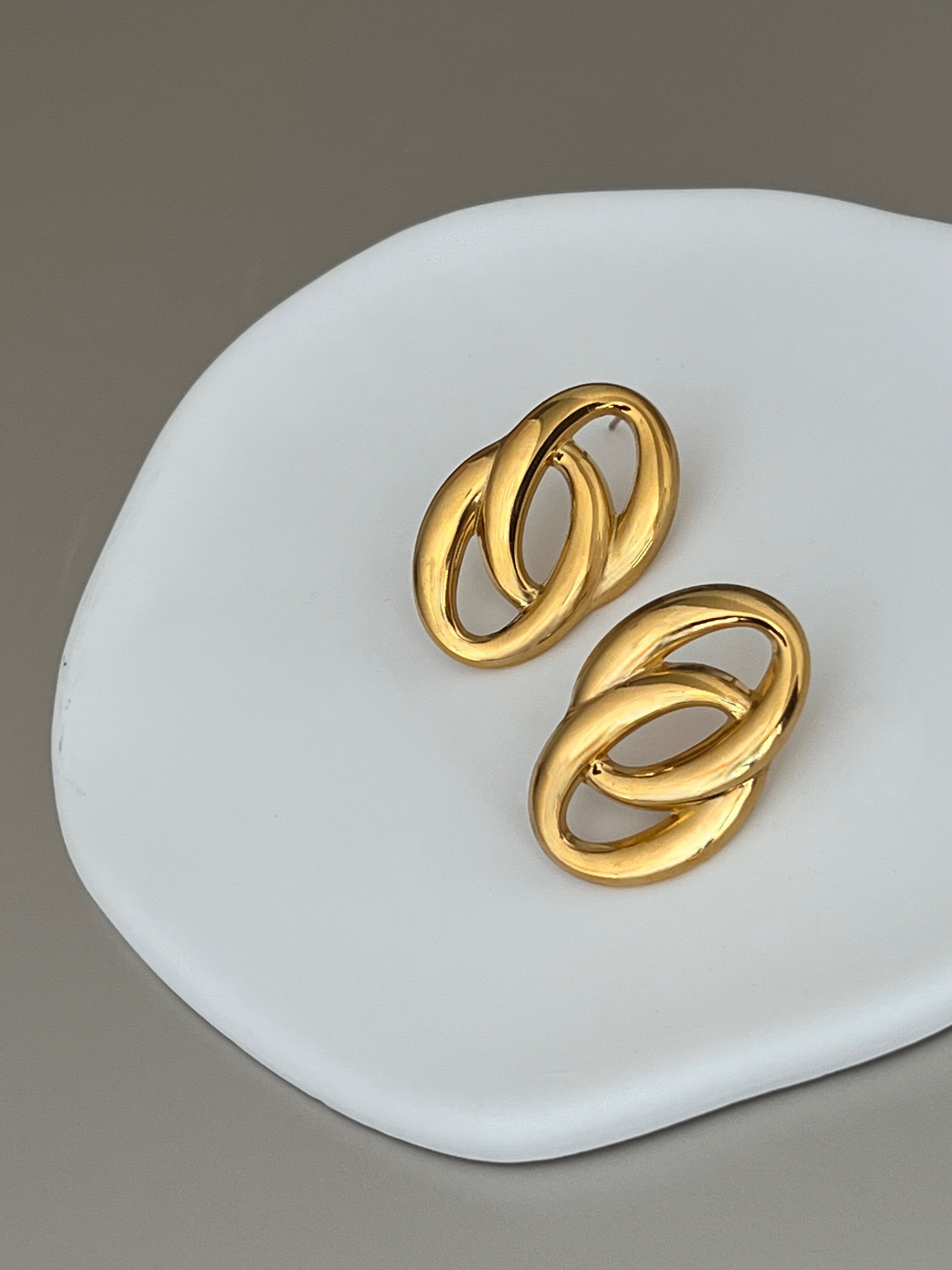 Pair of gold earrings on a white dish with a gray background