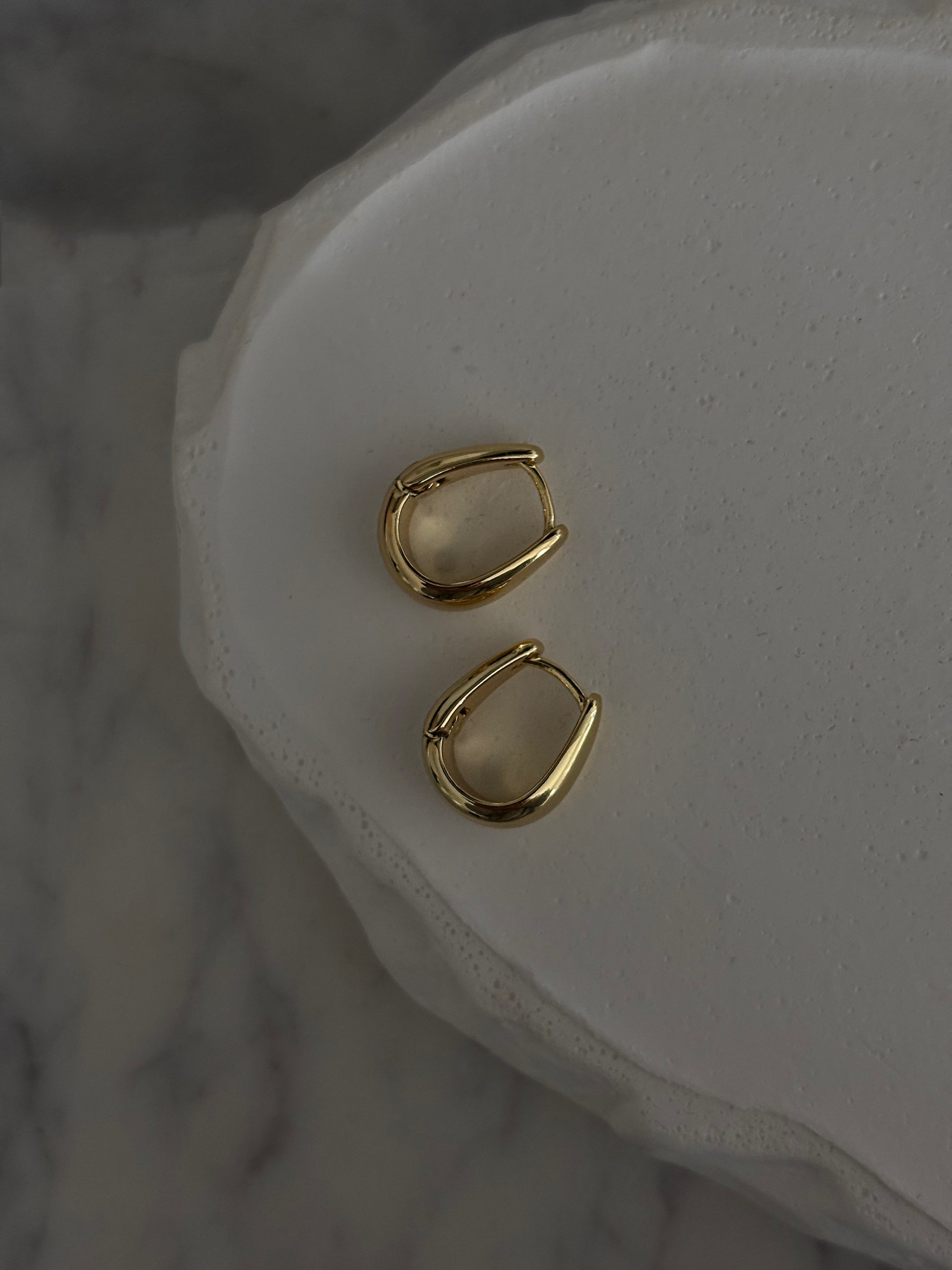 Gold hoop earrings on a white stone surface