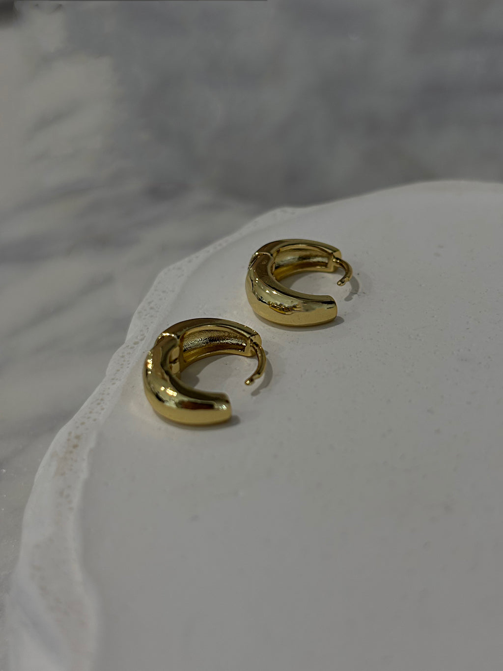 Gold hoop earrings on a white surface with a blurred background