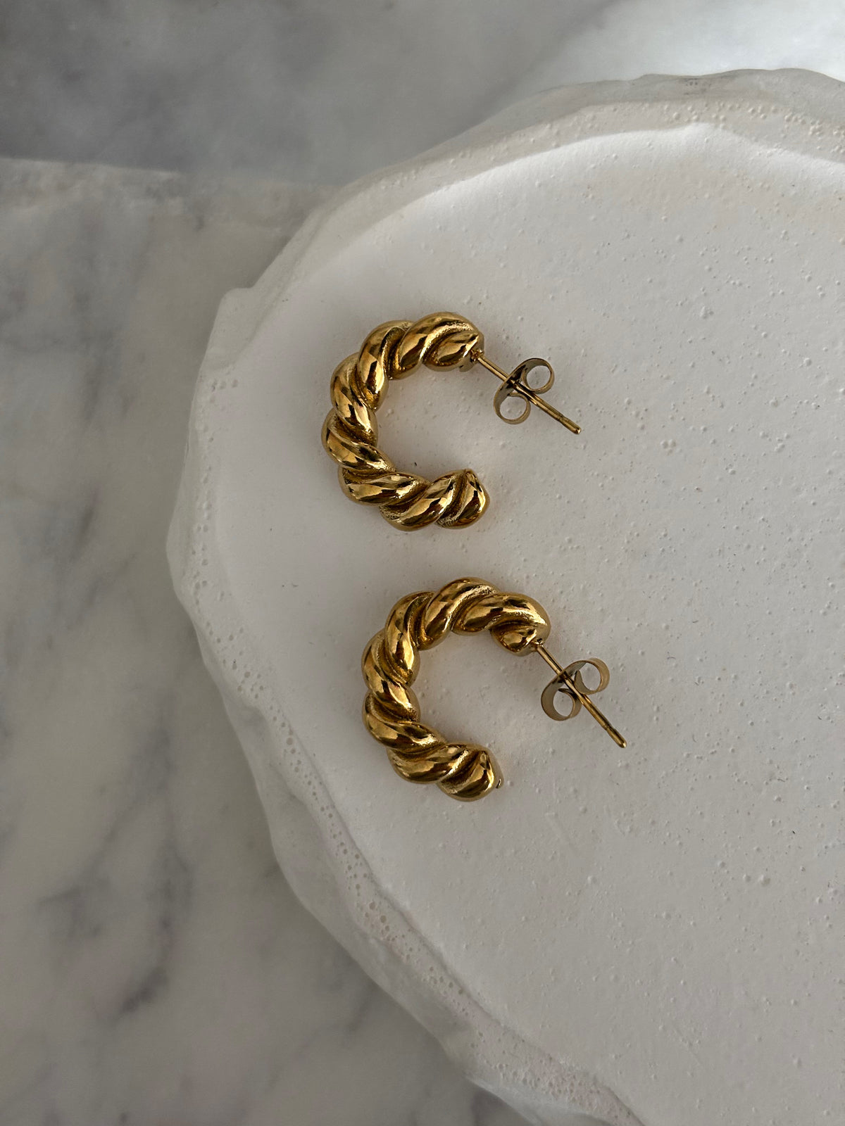 Gold hoop earrings on a white stone surface