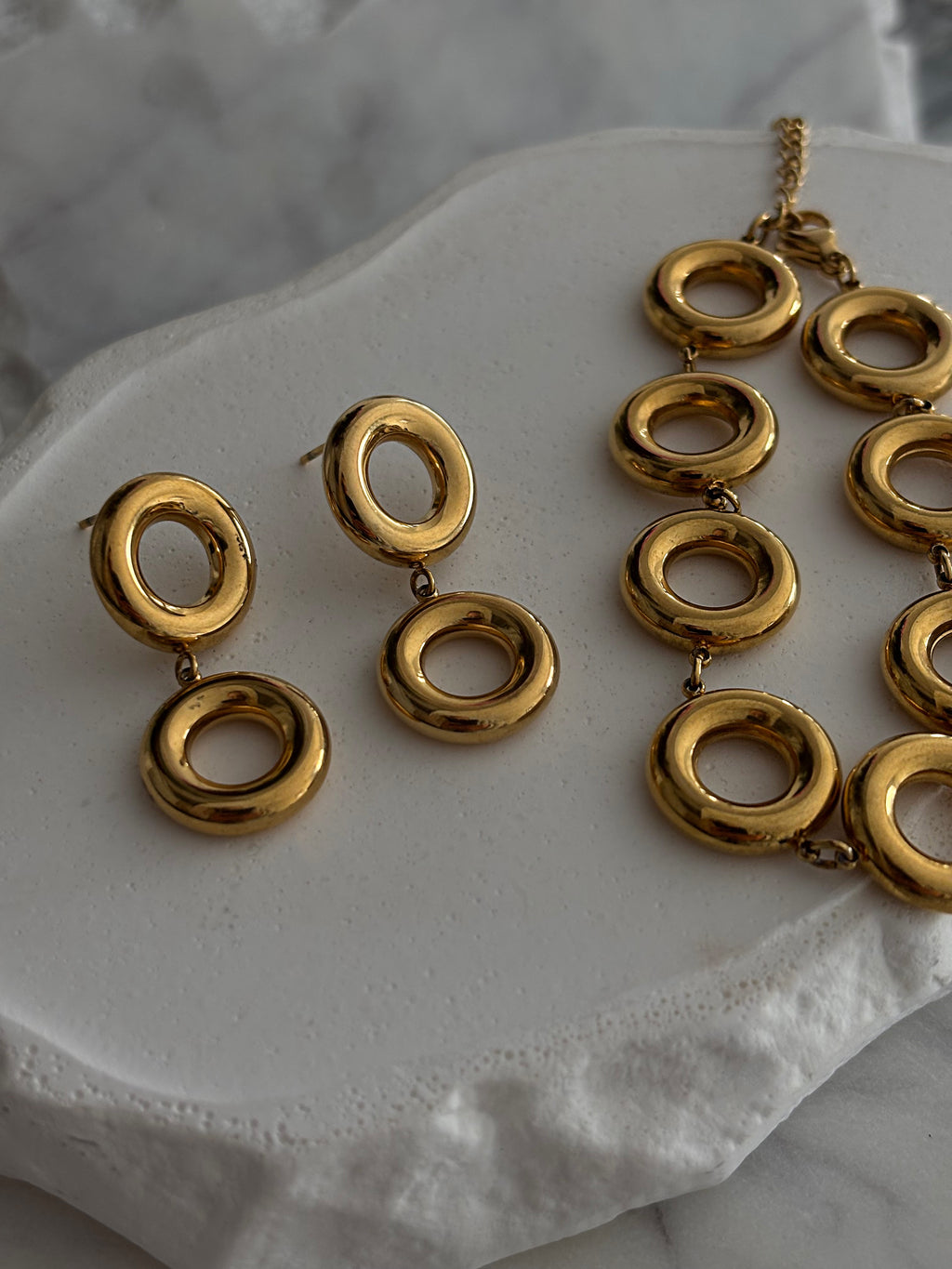 Gold everluxe necklace and earrings on a white surface