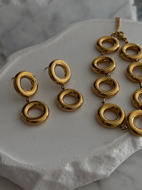 Gold everluxe necklace and earrings on a white surface
