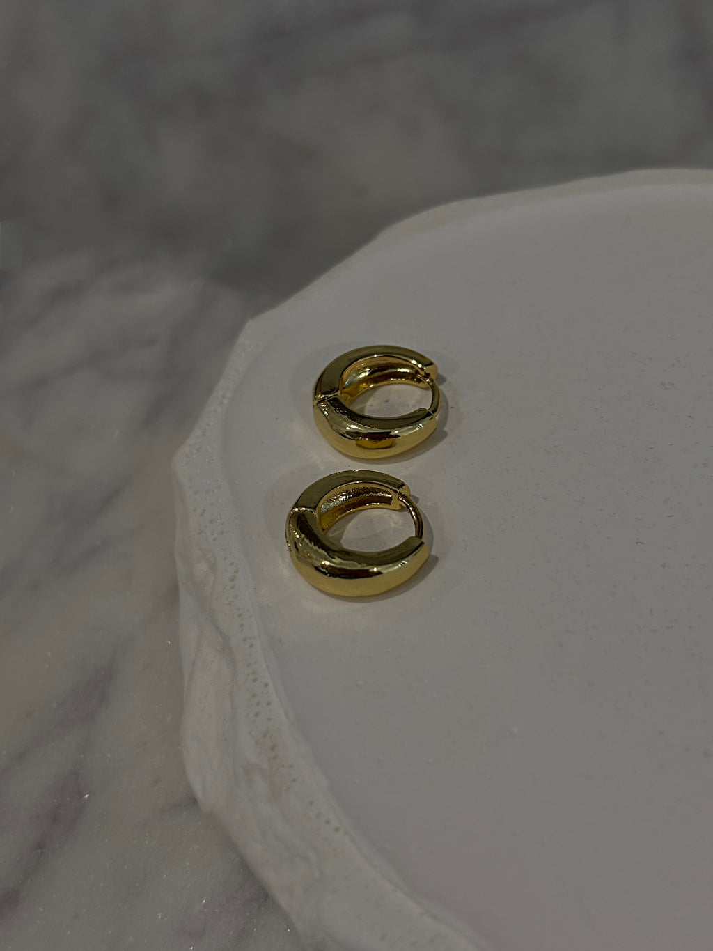 Gold hoop earrings on a white marble surface