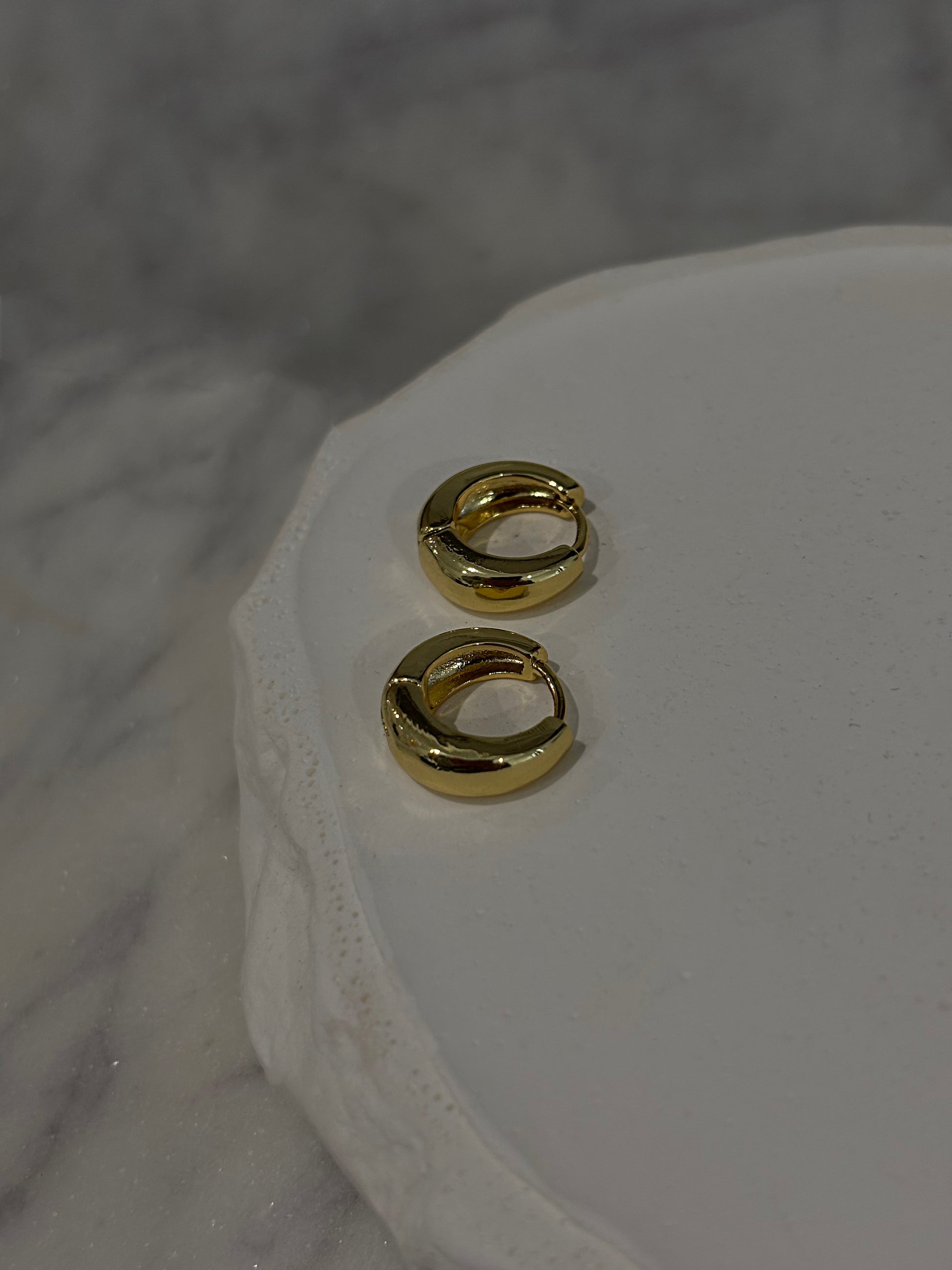 Gold hoop earrings on a white marble surface