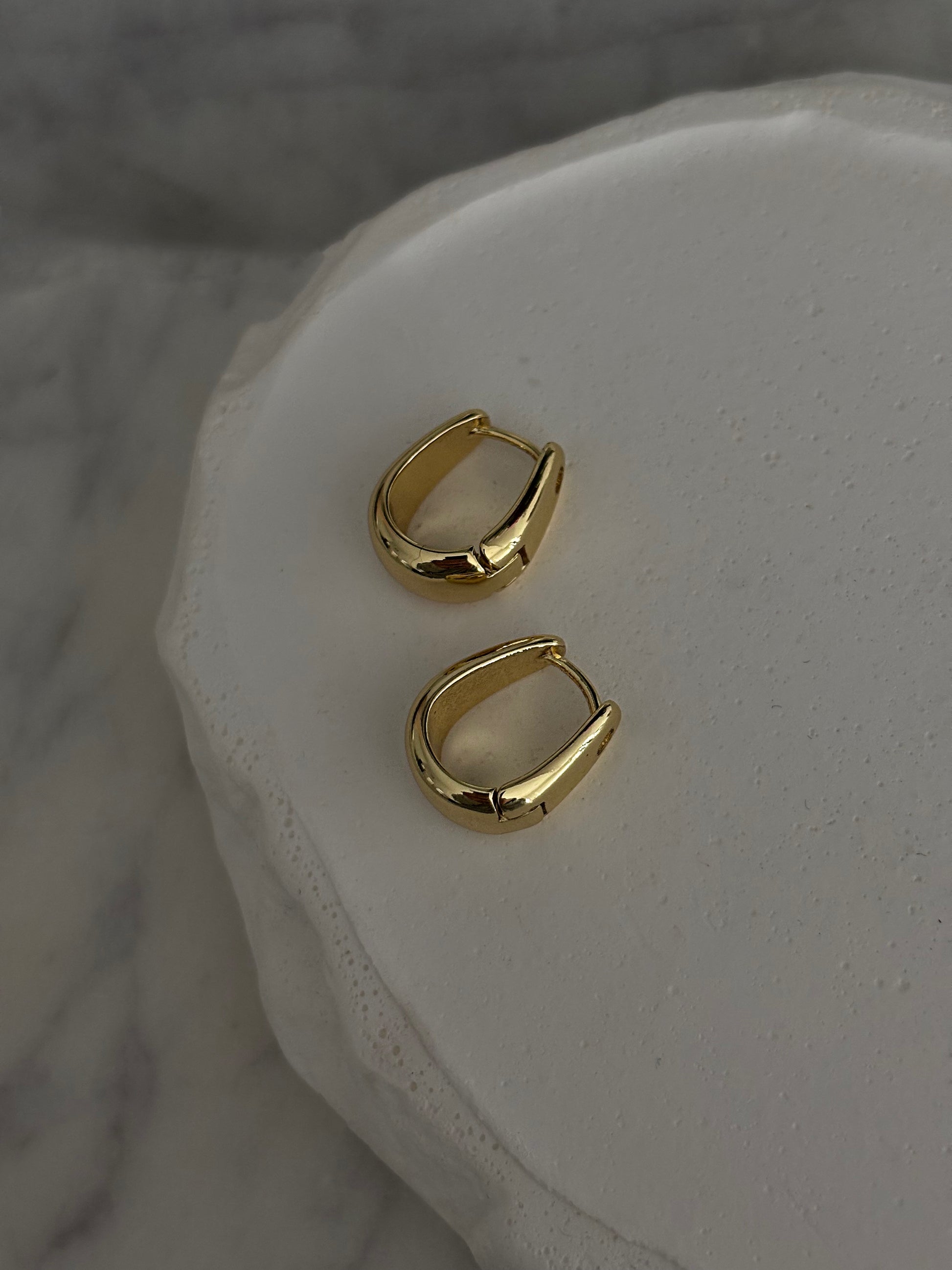 Gold hoop earrings on a white stone surface