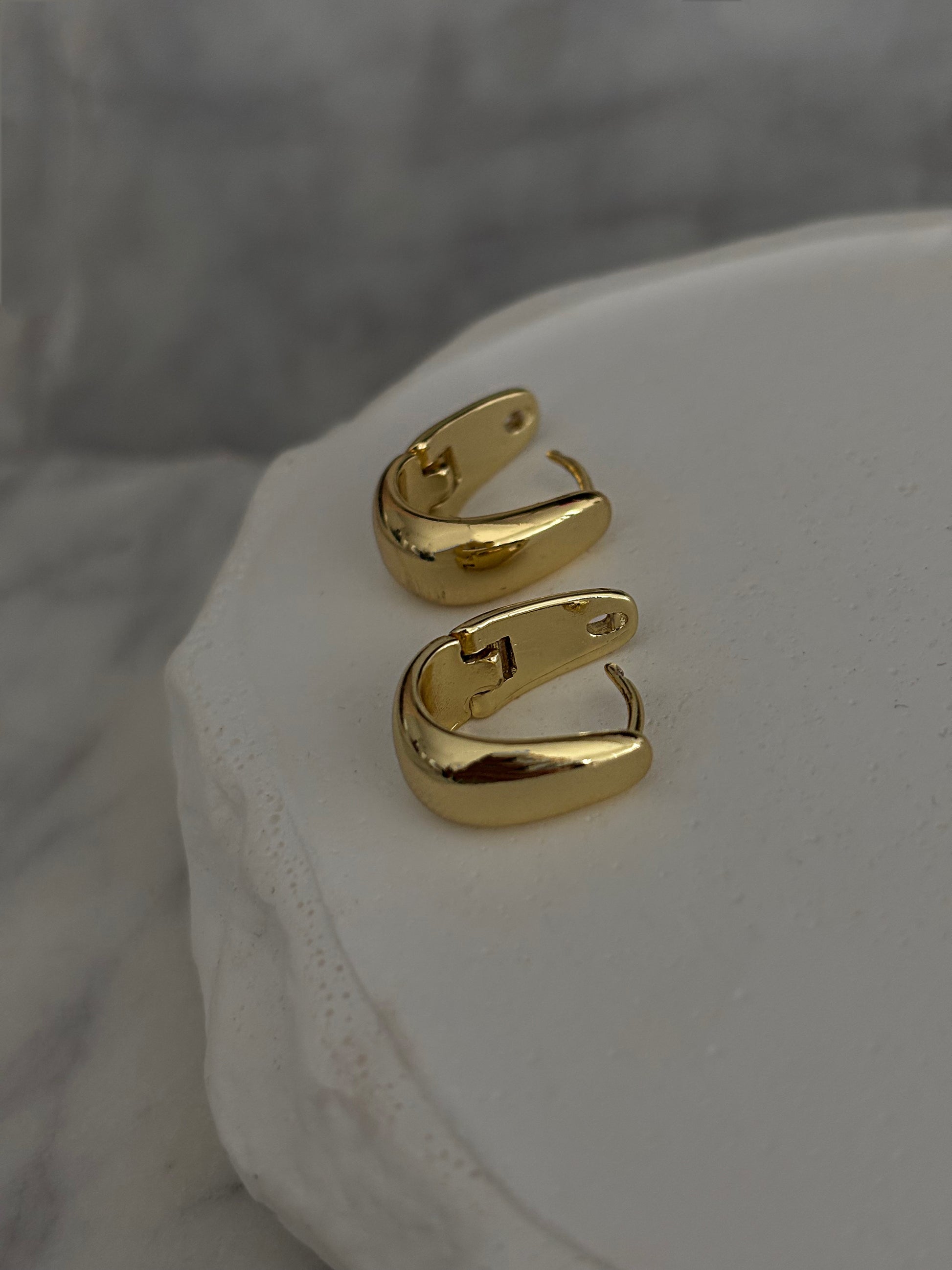 Gold hoop earrings on a white surface with a gray background