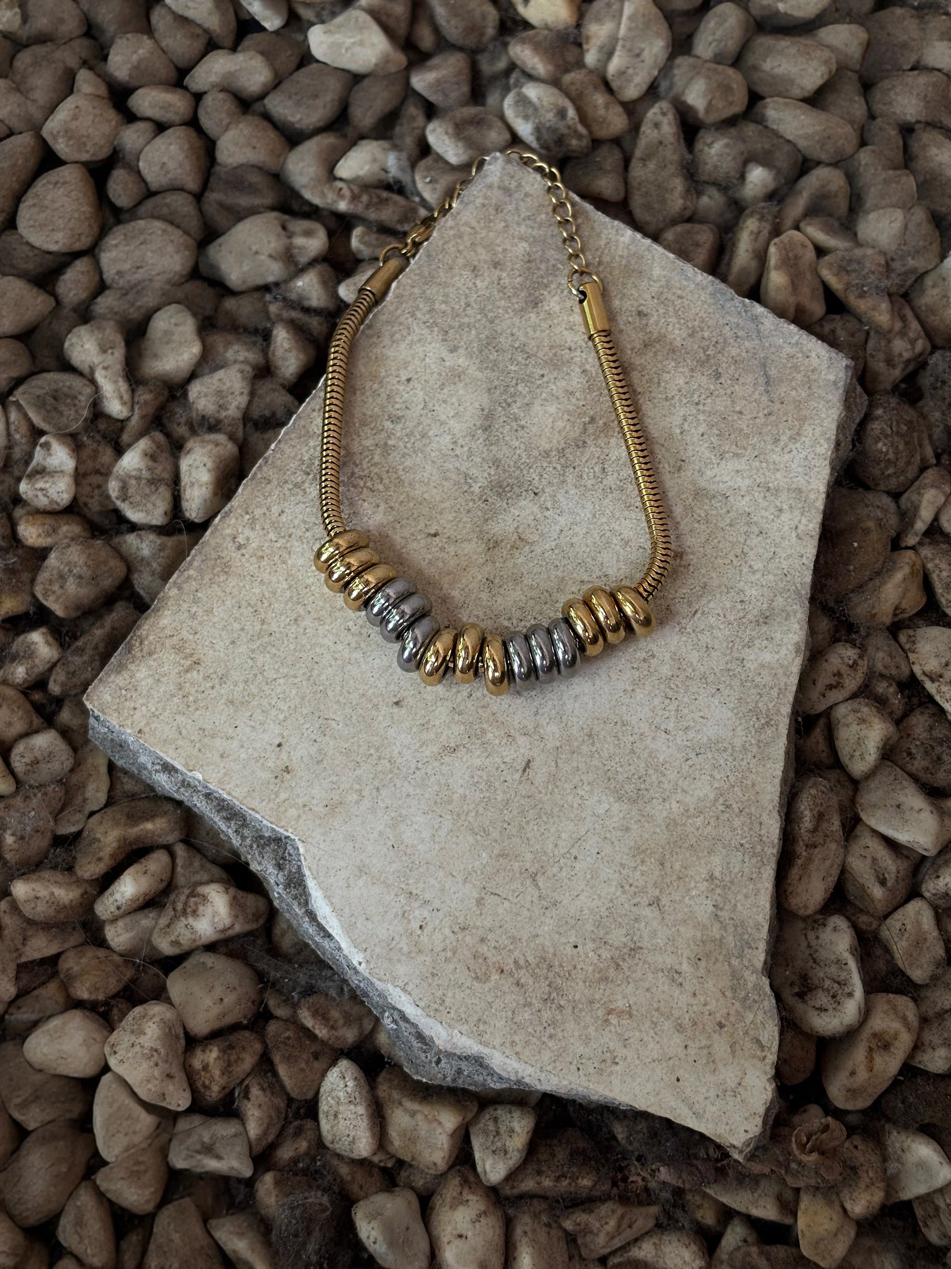 EverLuxe Eterna bracelet with gold and silver beads on a stone surface with pebbles in the background