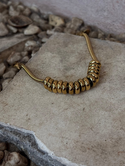 Gold waterproof beaded necklace on a stone surface with a natural stone background