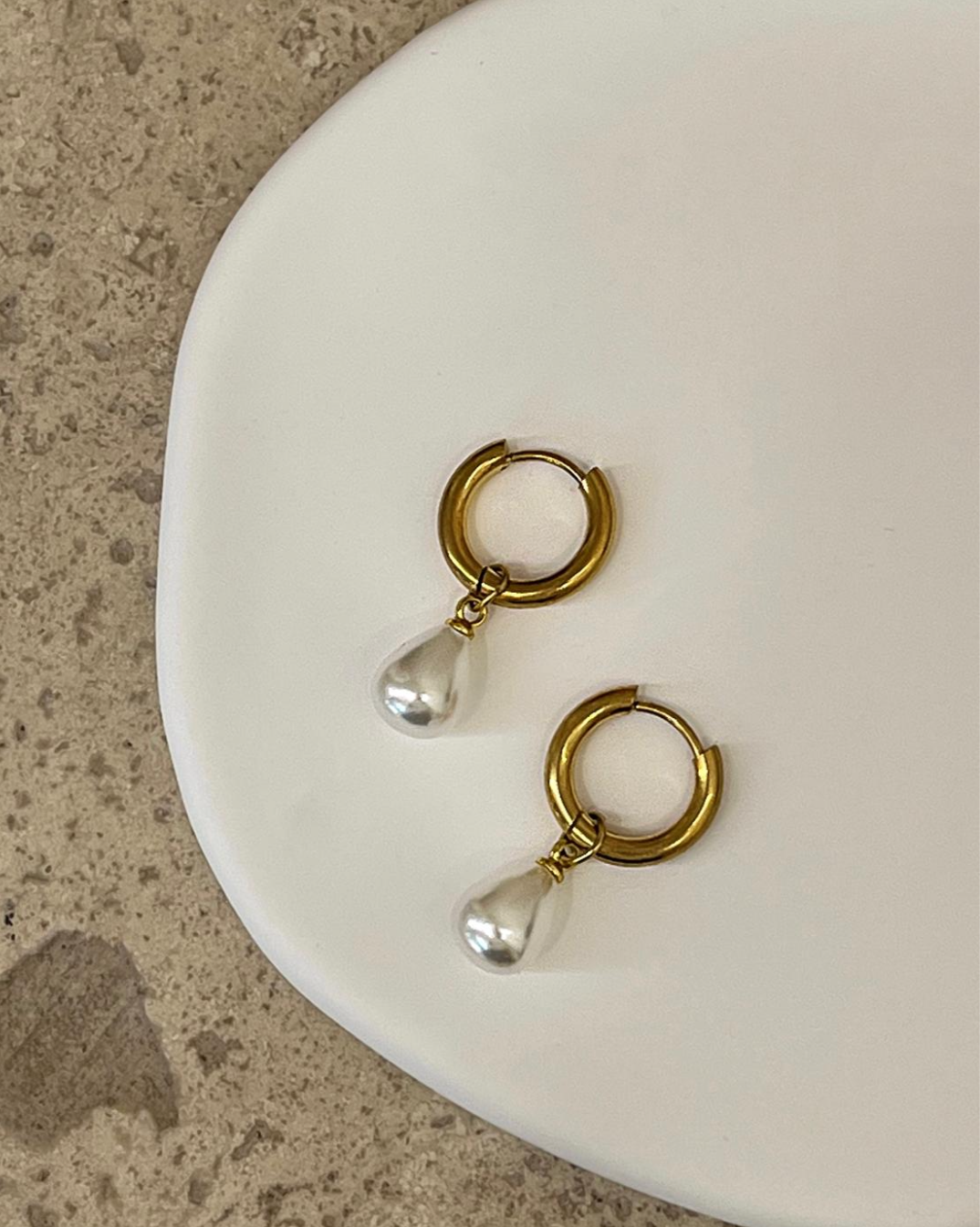 Pair of gold hoop earrings with clear teardrop stones on a white plate. Luna Drop by EverLuxe