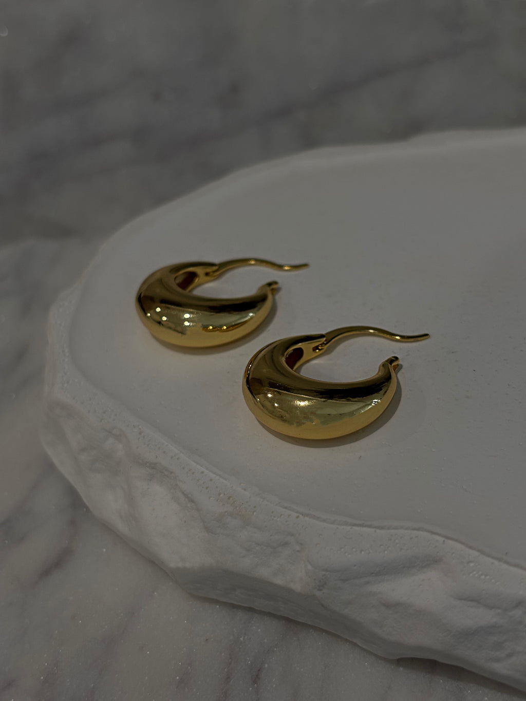 Gold hoop earrings on a textured white surface