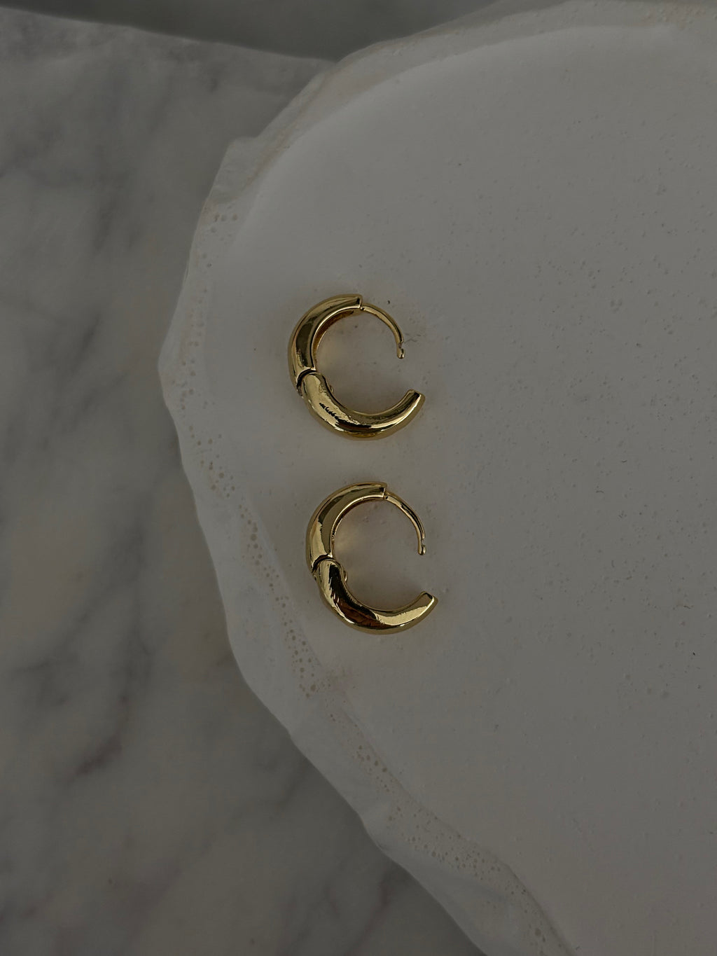 Gold hoop earrings on a white marble surface