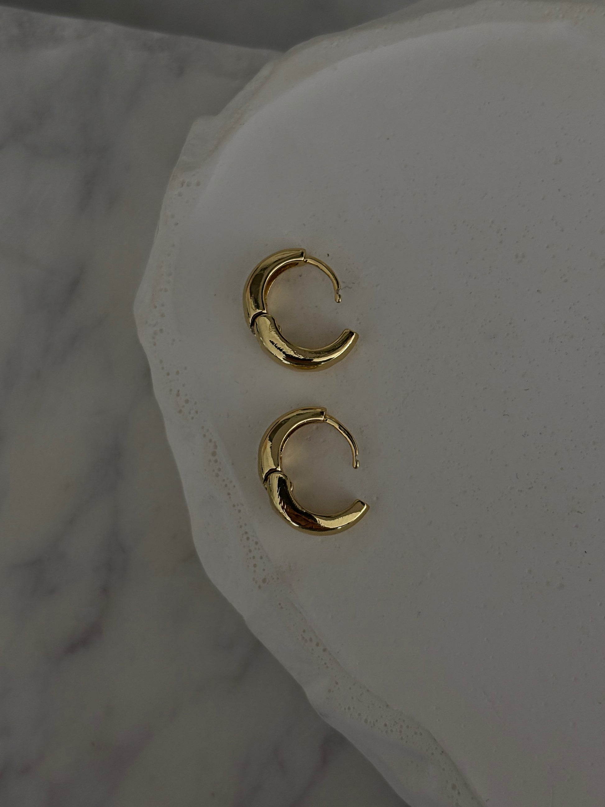 Gold hoop earrings on a white marble surface