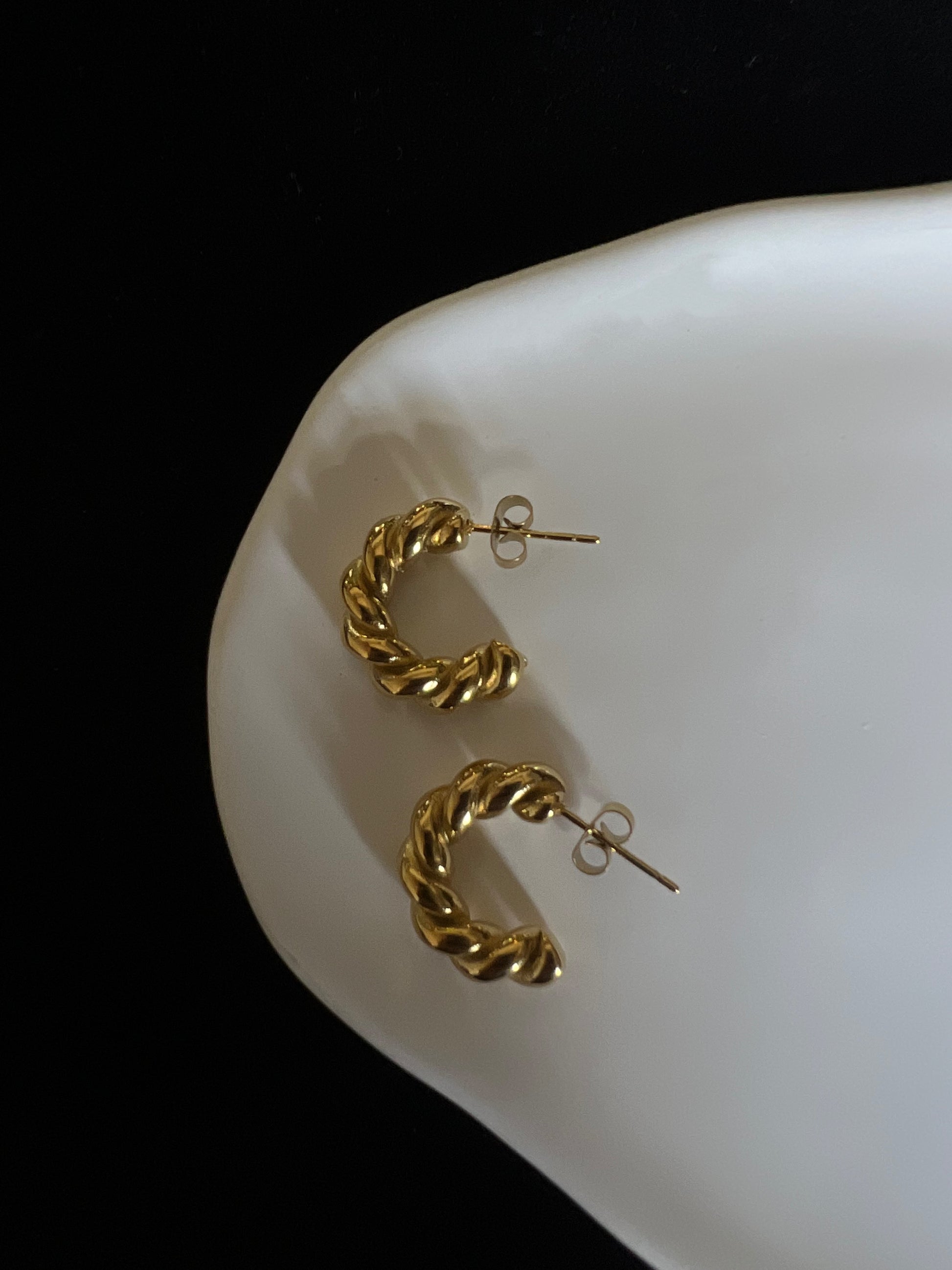 Gold rope twist earrings on a white dish with a black background
