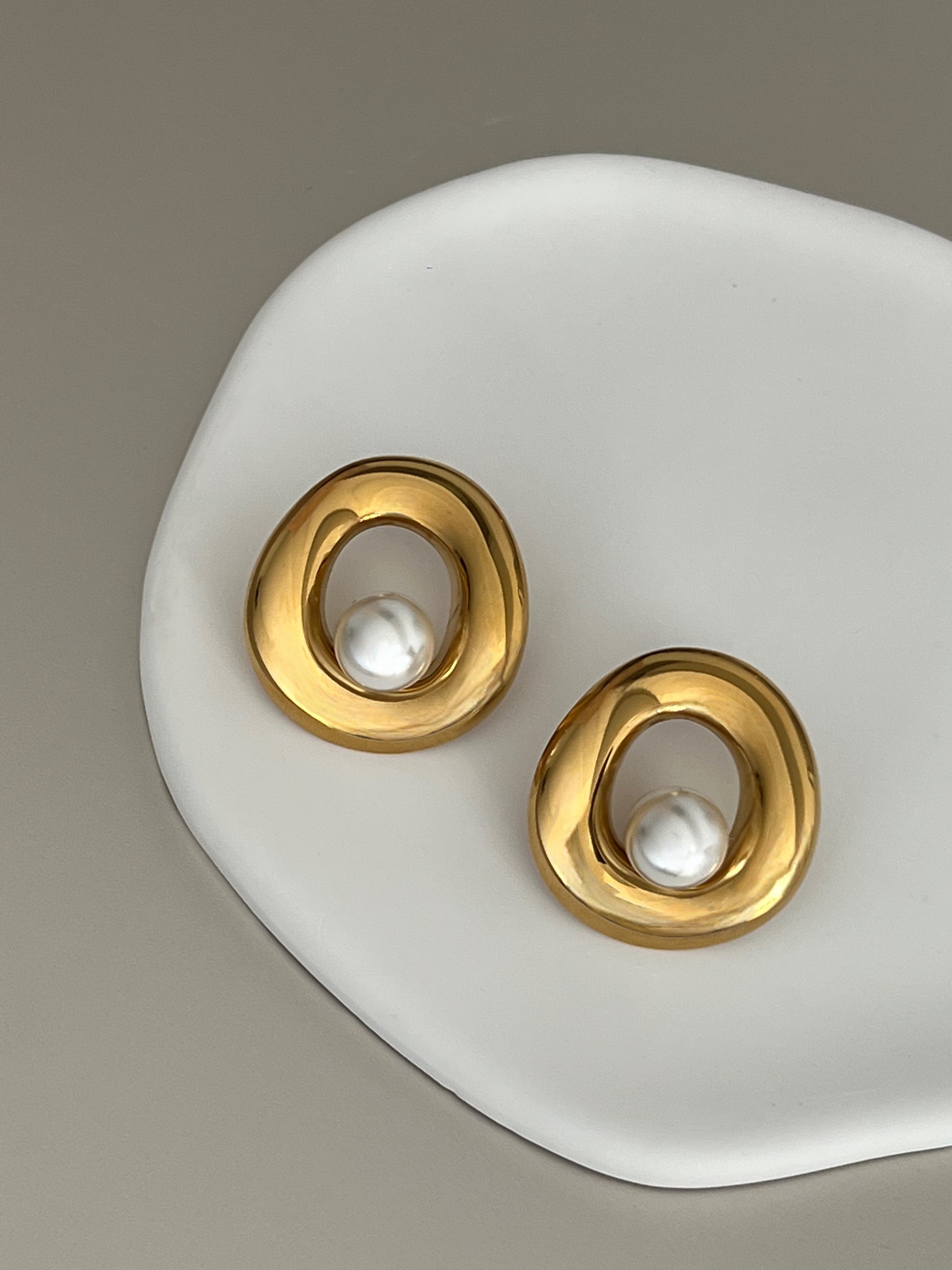 Gold earrings with pearl centers on a white stand against a gray background.