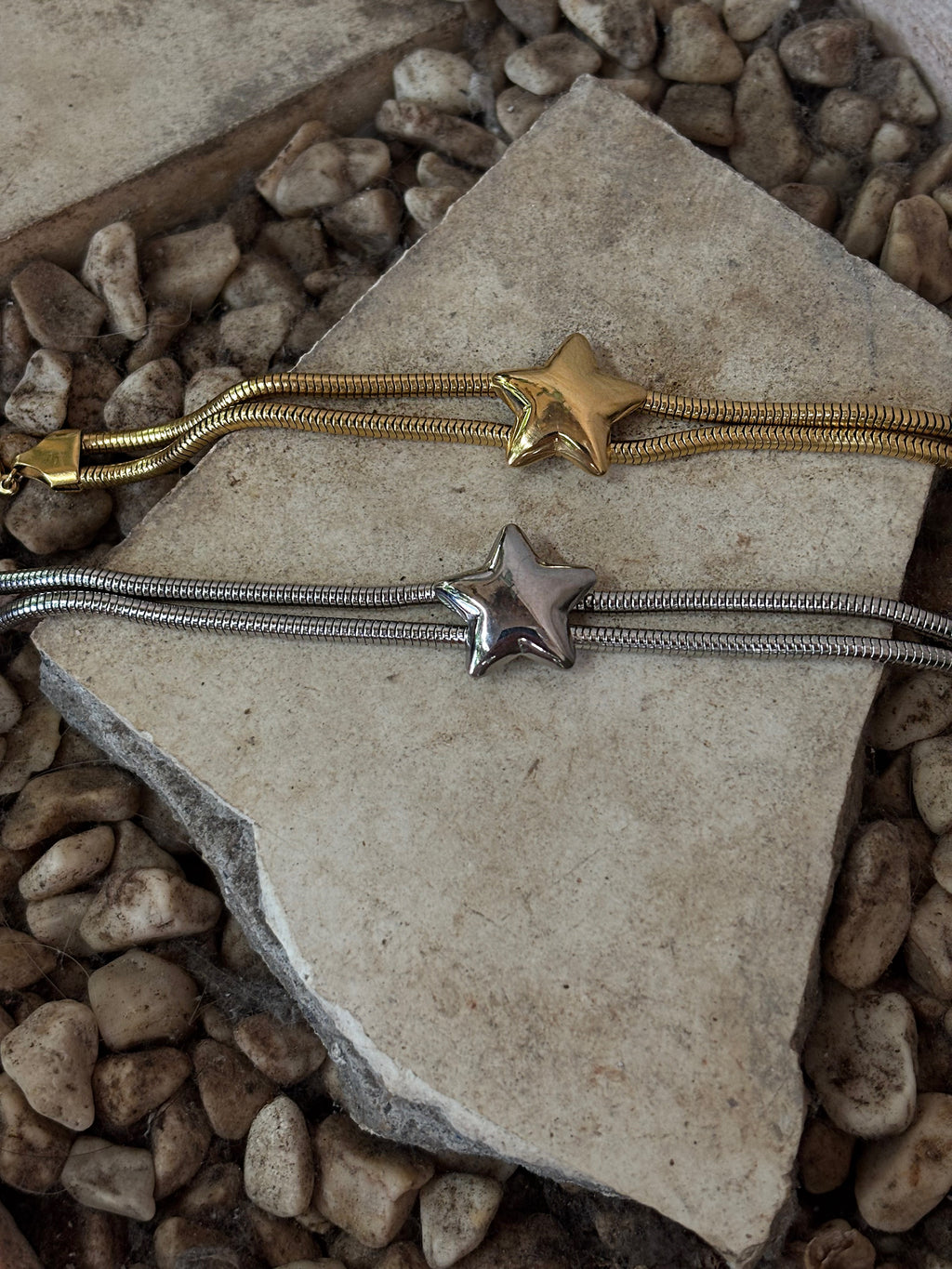 Two star-shaped bracelet ends on a stone surface with pebbles in the background. Waterproof bracelets