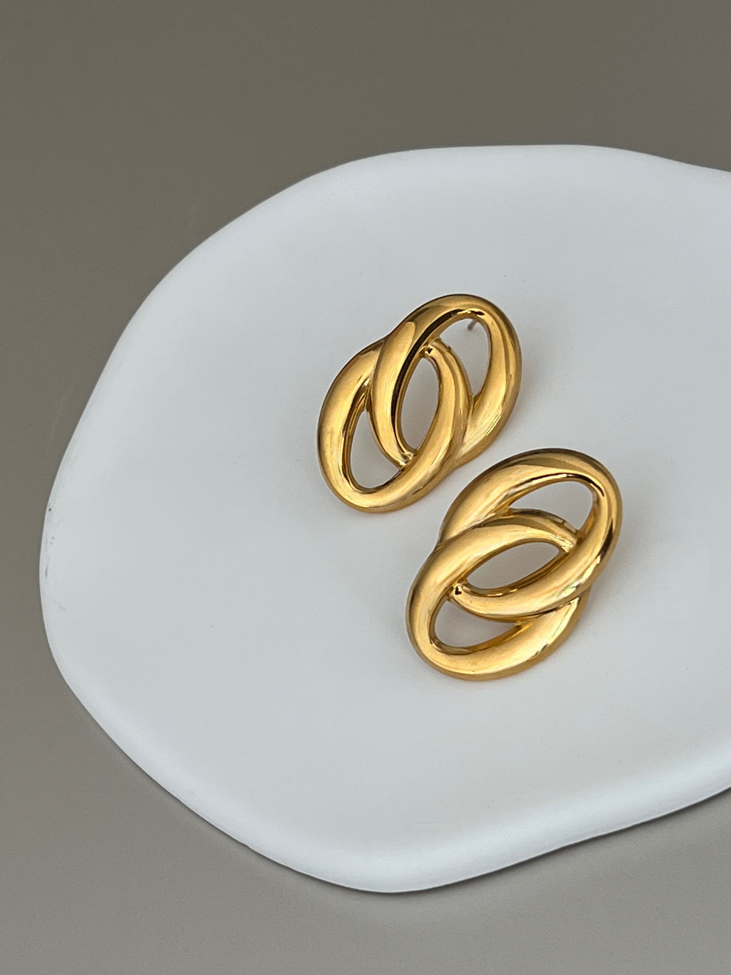 Pair of gold earrings on a white dish with a gray background